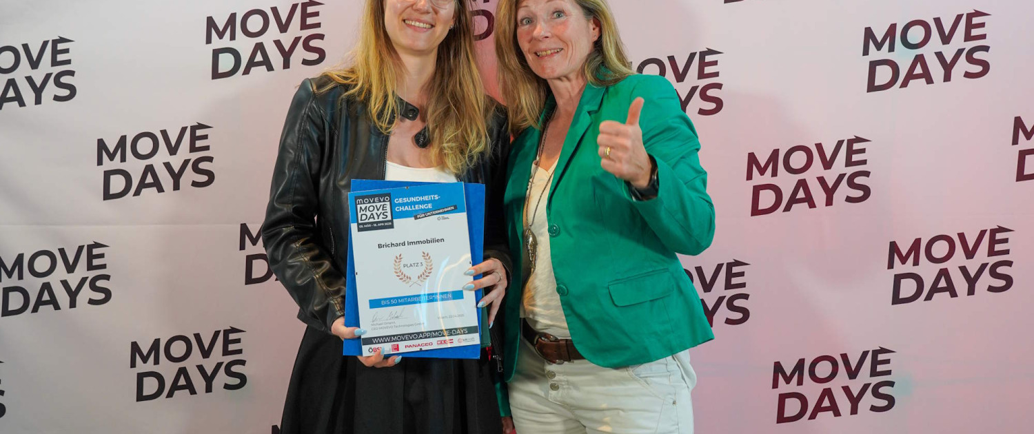 brichard-move-days-auszeichnung Zwei Frauen mit Zertifikat von Move Days vor einer Wand mit dem Logo Move Days