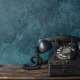 Vintage old black rotary phone with dust and scratches against a shabby wall with place for text. Concept of outdated communication technologies at home and office using an old telephone